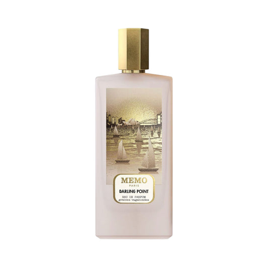 Frosted light pink rectangular perfume bottle with a gold-toned cap and an illustrated label depicting a golden cityscape wit