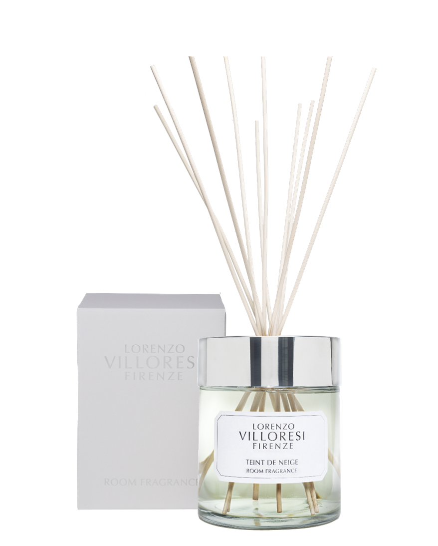 A luxury room fragrance set by Lorenzo Villoresi Firenze. The image features a clear glass diffuser jar filled with pale liquid and several natural wood reeds fanning out from a polished silver collar. The jar label and the accompanying minimalist white presentation box both feature the brand name and "TEINT DE NEIGE ROOM FRAGRANCE" in elegant black typography.