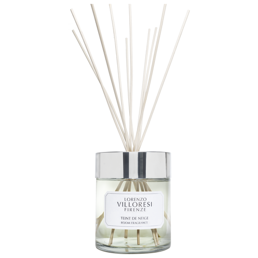 A luxury room fragrance set by Lorenzo Villoresi Firenze. The image features a clear glass diffuser jar filled with pale liquid and several natural wood reeds fanning out from a polished silver collar. The jar label and the accompanying minimalist white presentation box both feature the brand name and "TEINT DE NEIGE ROOM FRAGRANCE" in elegant black typography.