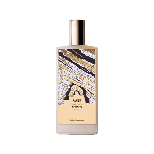 A white bottle of Memo Paris Zante Eau de Parfum standing next to its tan textured presentation box. The bottle features a colorful, abstract illustration of coastal rock formations.