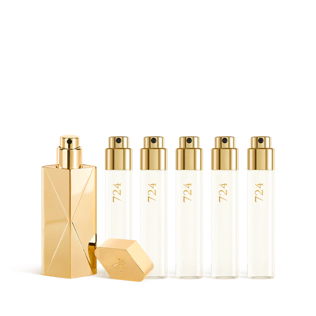 A luxury fragrance travel set featuring a sculptural gold travel spray case alongside five clear 11ml glass perfume refills labeled "724" with gold spray nozzles.