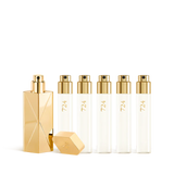 A luxury fragrance travel set featuring a sculptural gold travel spray case alongside five clear 11ml glass perfume refills labeled "724" with gold spray nozzles.