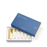The Maison Francis Kurkdjian 724 travel set displayed in an open blue presentation box with gold lettering, neatly housing the gold Globe Trotter case and five 11ml refills.