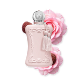 A 75ml bottle of Parfums de Marly Delina perfume in pastel pink, artfully surrounded by blossoming pink roses and fresh lychee fruits.