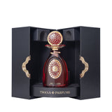 Dark red perfume bottle with an ornate gold-toned cap and label, presented in a black textured box with gold-toned clasps.