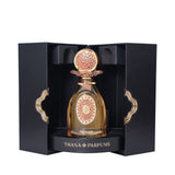 Black box with gold-toned trim holds an amber perfume bottle. It has a gold-toned cap with coral-pink texture and an ornate g