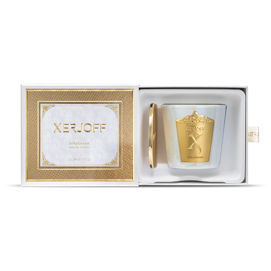 A luxury Xerjoff SilkyGreen scented candle and its gold lid nestled inside a white presentation box with a gold textured frame and satin pull tab.