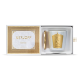 A luxury Xerjoff SilkyGreen scented candle and its gold lid nestled inside a white presentation box with a gold textured frame and satin pull tab.