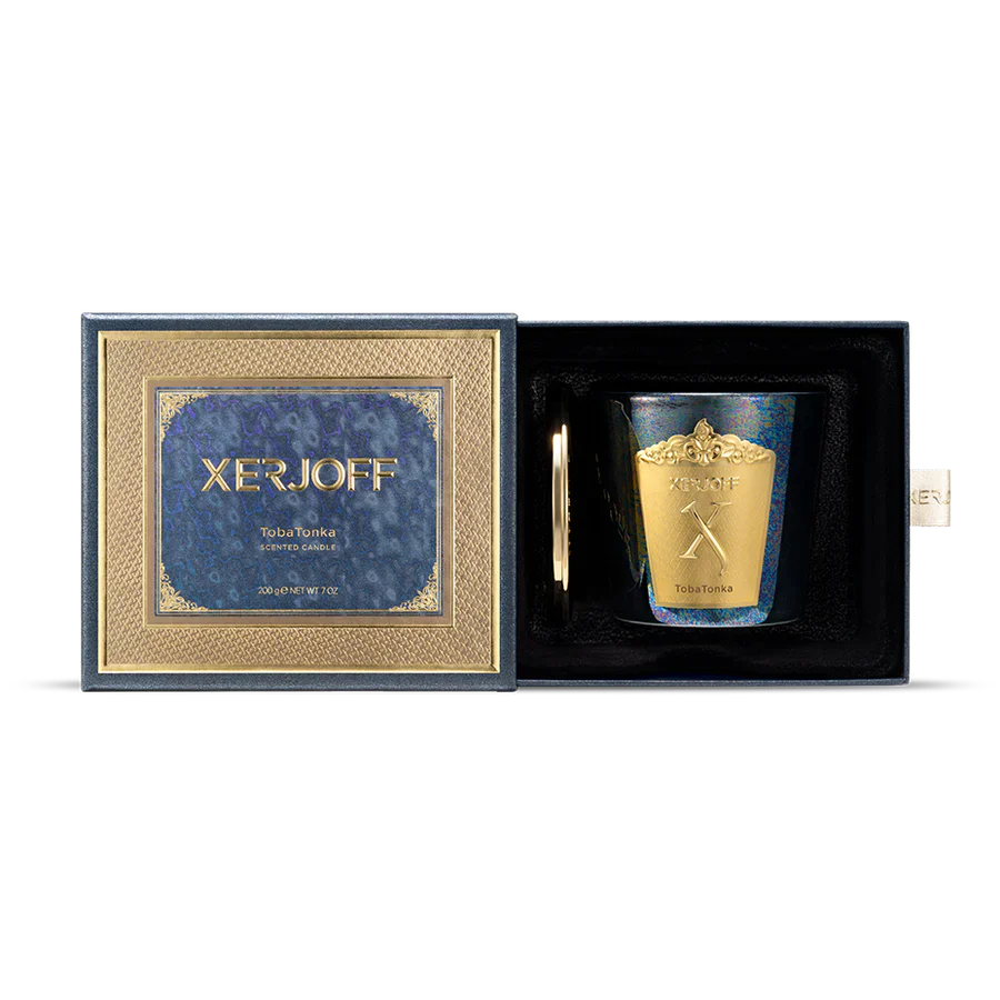 An iridescent, dark-toned glass candle holder with vibrant blue and green shifts, adorned with a large gold Xerjoff crest, shown next to a polished gold lid.