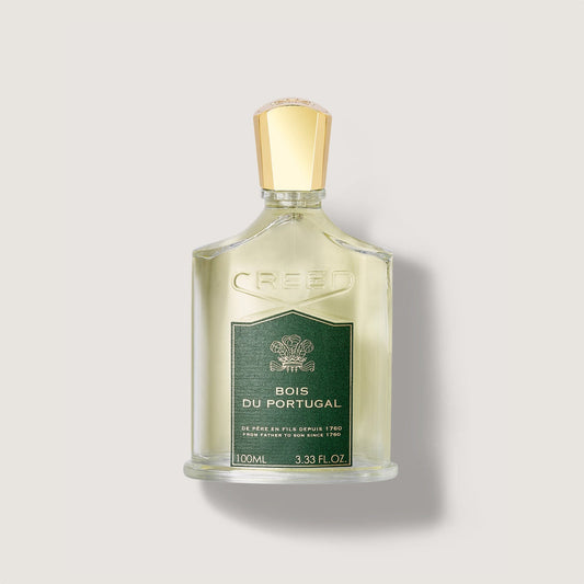 Rectangular clear glass fragrance bottle with light yellow liquid, a dark green label, and a gold-toned cap. 'CREED' is embos